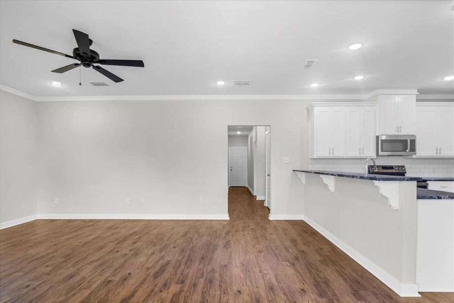 Kitchen with appliances with stainless steel finishes, white cabinets, open floor plan, dark wood-type flooring, and ornamental molding