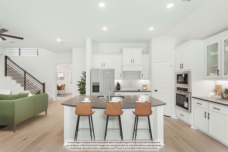 Open kitchen with white cabinets, dark island with three bar stools, and stainless steel appliances