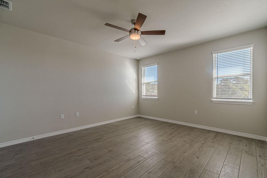 Empty room featuring healthy amount of natural light, wood finished floors, and ceiling fan Empty room featuring healthy amount of natural light, wood finished floors, and ceiling fan