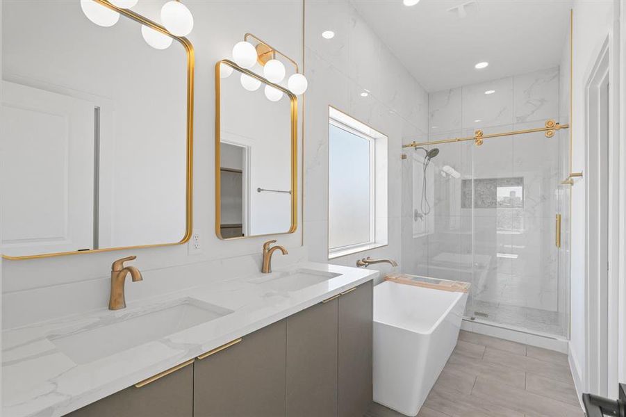 Highlighting an amazing glass enclosed shower with gorgeous tile, a beautiful free standing tub, a large window that lets in plenty of natural light, recessed lighting, double sinks, quartz countertops, and framed mirrors.