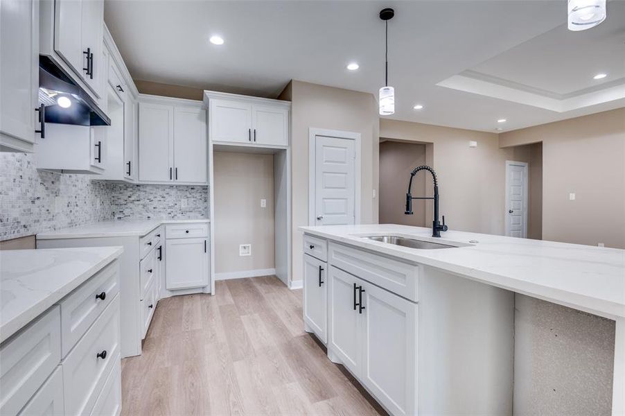 Kitchen with pendant lighting, a sink, light stone counters, under cabinet range hood, and backsplash