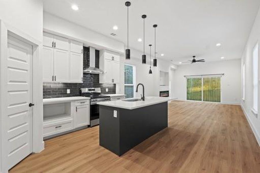 Kitchen featuring stainless steel range with electric stovetop, ceiling fan, a kitchen island with sink, wall chimney range hood, and white cabinetry