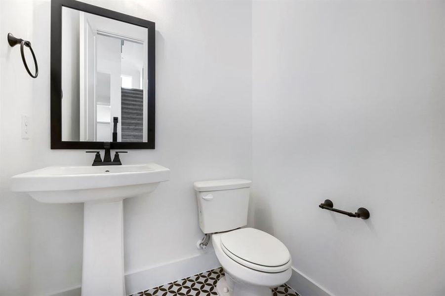 Modern powder room featuring a white pedestal sink with matte black faucet, a framed mirror, and a toilet Modern powder room featuring a white pedestal sink with matte black faucet, a framed mirror, and a toilet