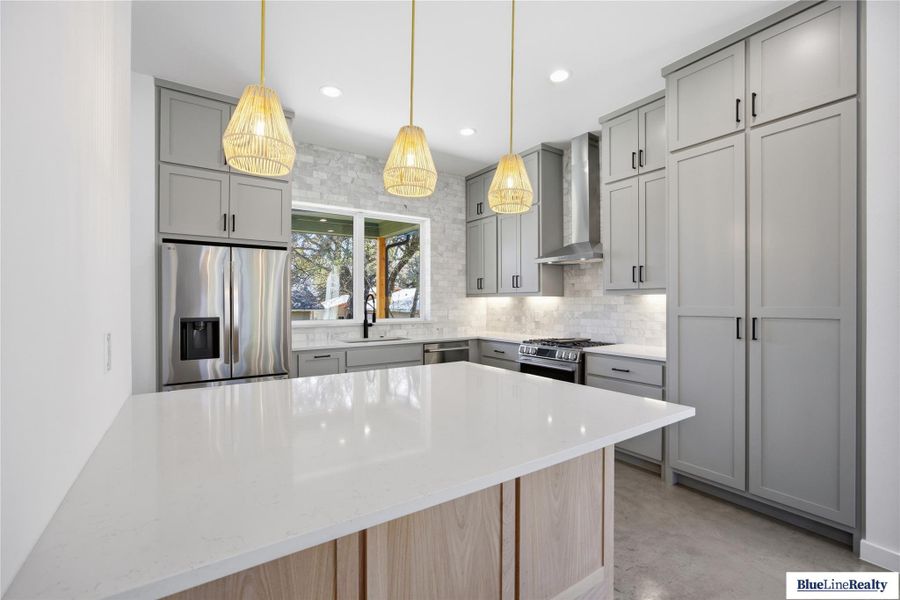 Kitchen with gray cabinets, light stone counters, and stainless steel appliances