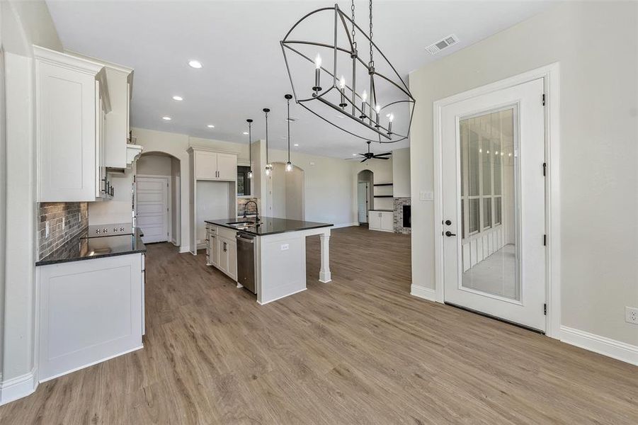 Kitchen featuring a kitchen island with sink, light hardwood / wood-style flooring, backsplash, decorative light fixtures, and dishwasher