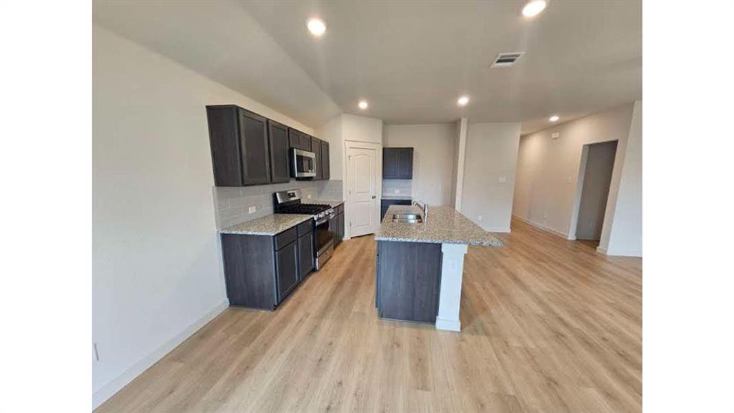 Kitchen featuring dark wood-finish cabinetry, light speckled countertops, and stainless steel appliances Kitchen featuring dark wood-finish cabinetry, light speckled countertops, and stainless steel appliances
