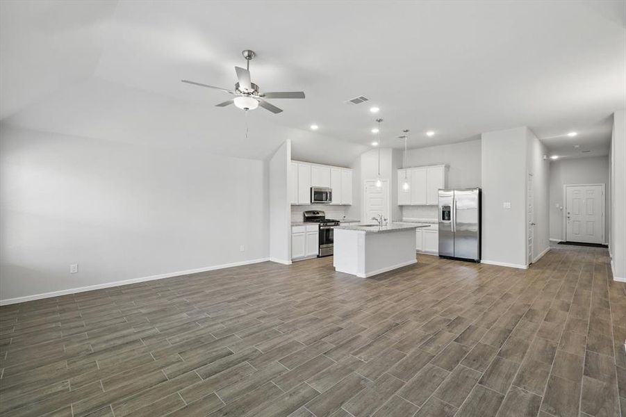 Kitchen with appliances with stainless steel finishes, open floor plan, ceiling fan, a kitchen island with sink, and vaulted ceiling Kitchen with appliances with stainless steel finishes, open floor plan, ceiling fan, a kitchen island with sink, and vaulted ceiling