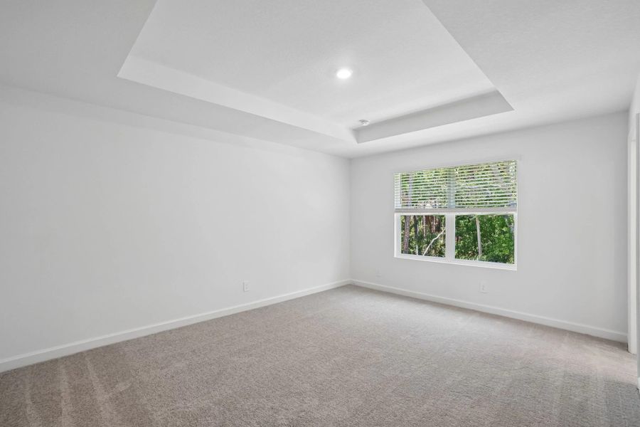 Primary bedroom with a tray ceiling looking out into the tree filled back view