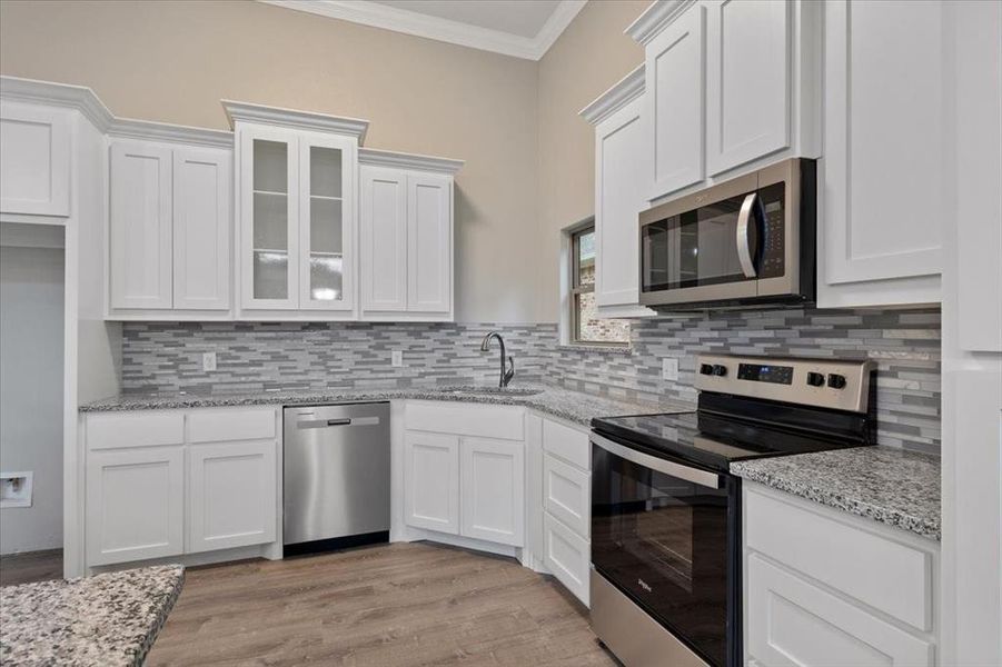 Kitchen with stainless steel appliances, backsplash, light hardwood / wood-style flooring, and sink