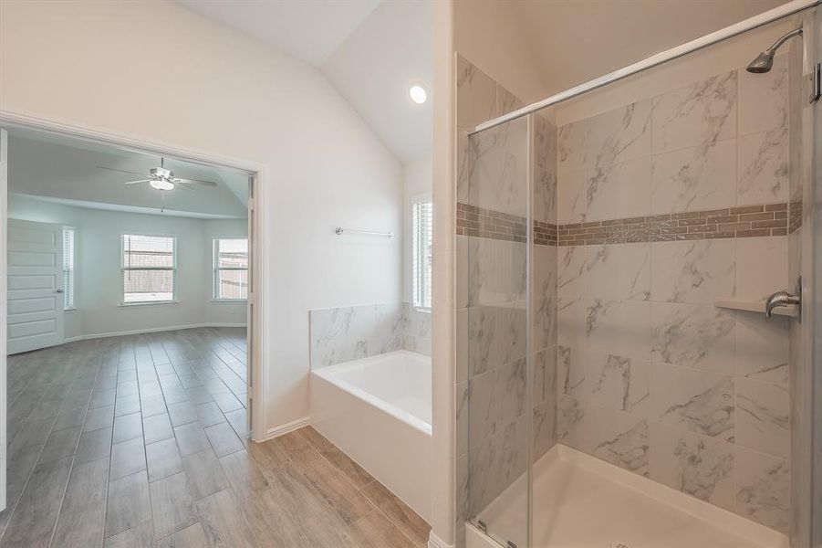Bathroom with a marble finish shower, a garden tub, wood tiled floors, vaulted ceiling, and a ceiling fan Bathroom with a marble finish shower, a garden tub, wood tiled floors, vaulted ceiling, and a ceiling fan