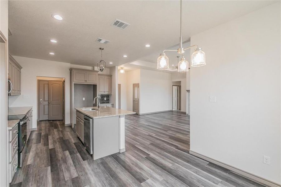 Kitchen featuring light stone countertops, decorative light fixtures, a center island with sink, stainless steel appliances, and recessed lighting