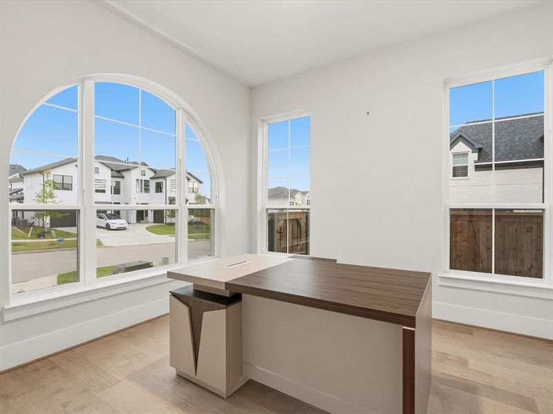 Bright room featuring a large arched window with multiple panes, two additional rectangular windows, wood-finish flooring, and white baseboards Bright room featuring a large arched window with multiple panes, two additional rectangular windows, wood-finish flooring, and white baseboards