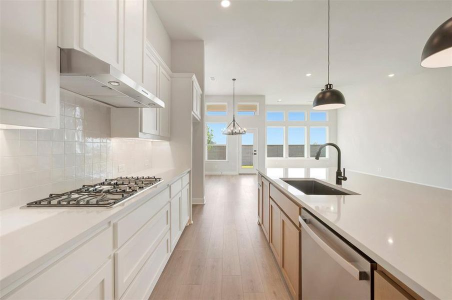 Modern kitchen featuring white shaker cabinetry, stainless steel range hood, built-in gas cooktop, and a large central island with an integrated sink and black faucet