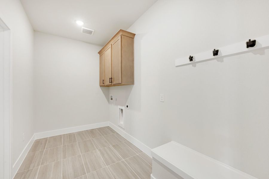 Laundry and mudroom area with wood upper cabinet, wall hooks, built-in bench, and light tile flooring