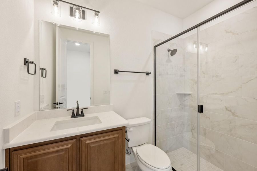 Bathroom with wood vanity, white countertop, and glass-enclosed marble tile shower