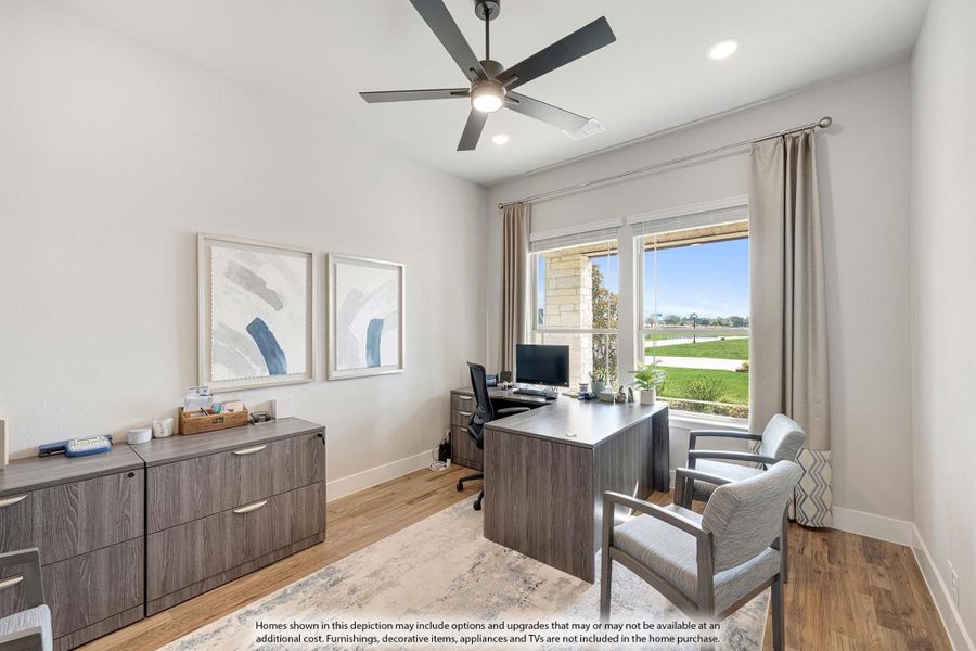 Home office with wood desk, ceiling fan, hardwood floors, and large window with backyard view