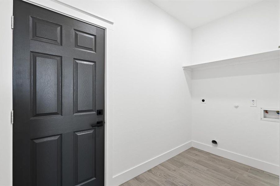 This is a modern, clean space featuring a dark door set against white walls, with light gray wood-patterned flooring. There's a recessed nook with outlets, potentially for laundry appliances or storage.