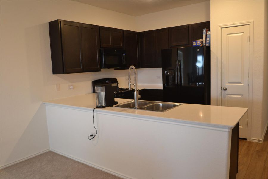 Kitchen featuring dark brown cabinets, black appliances, light countertops, and a peninsula