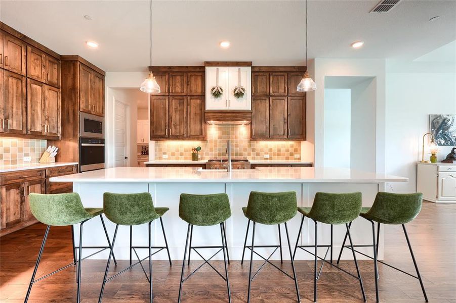 Kitchen featuring a breakfast bar area, a large island with sink, tasteful backsplash, hanging light fixtures, and stainless steel appliances