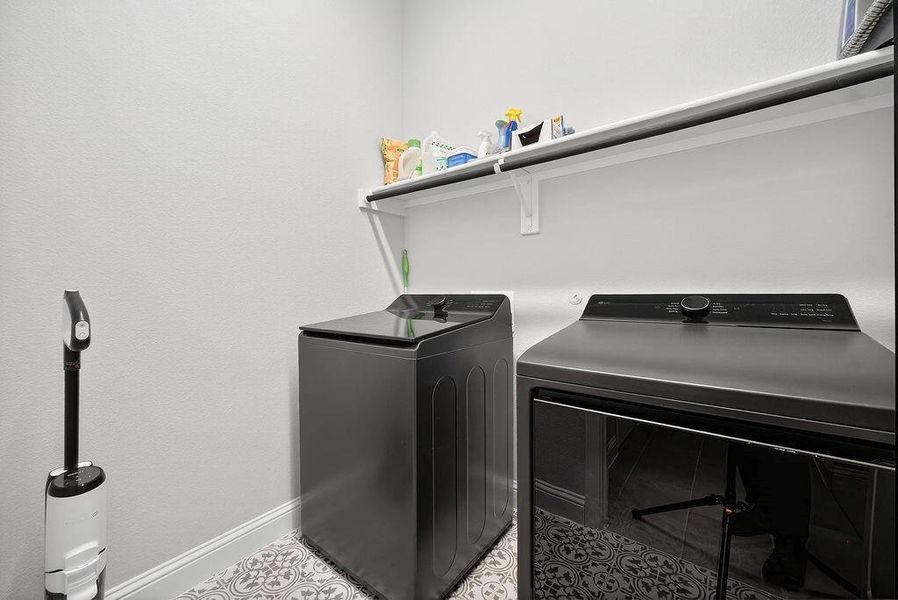 Utility space featuring patterned floor tile, white baseboards, and a white wall shelf with an integrated hanging rod