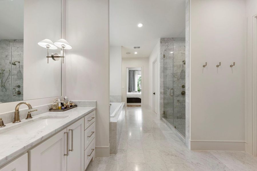 Elegant primary bath featuring marble flooring, a soaking tub, glass walk-in shower, and separate his-and-her vanities with marble countertops and designer fixtures.