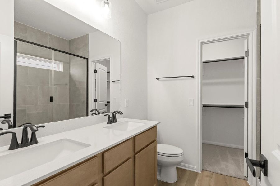 Full bathroom featuring a shower stall, double vanity, light wood-type flooring, and a spacious closet