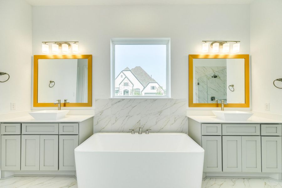 This view highlights the custom mirrors, elegant lighting, and the spacious soaking tub. The dual vanities offer ample cabinetry, complemented by modern, square-profile sinks.