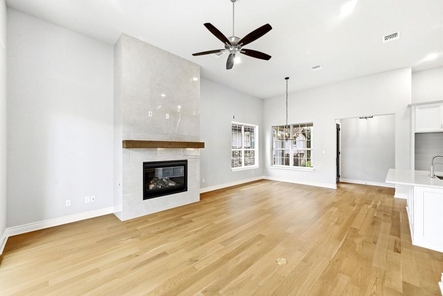 Spacious living area featuring a floor-to-ceiling tiled fireplace with a wood mantel, wood-finish flooring, and a ceiling fan