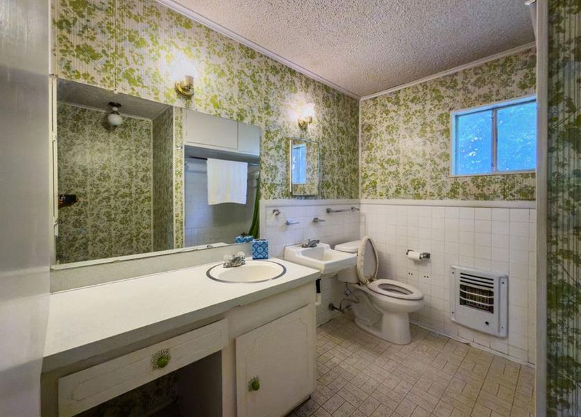 Bathroom featuring wallpapered walls, tile walls, heating unit, a textured ceiling, and ornamental molding