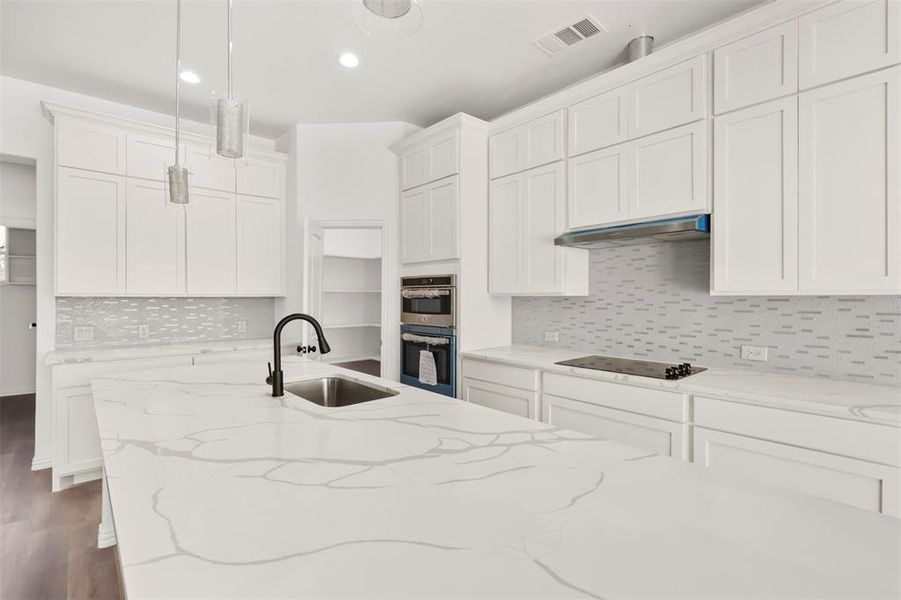 Kitchen with white cabinets, sink, hanging light fixtures, black electric cooktop, and double oven