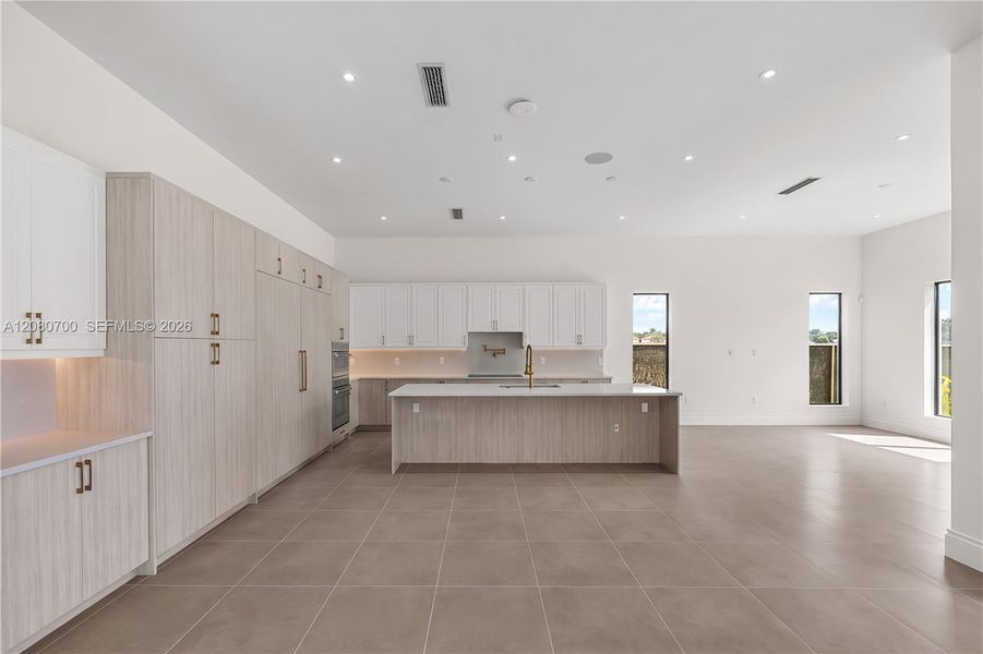 Spacious open-concept kitchen featuring an oversized island, tile flooring, built-in double oven, and recessed lighting