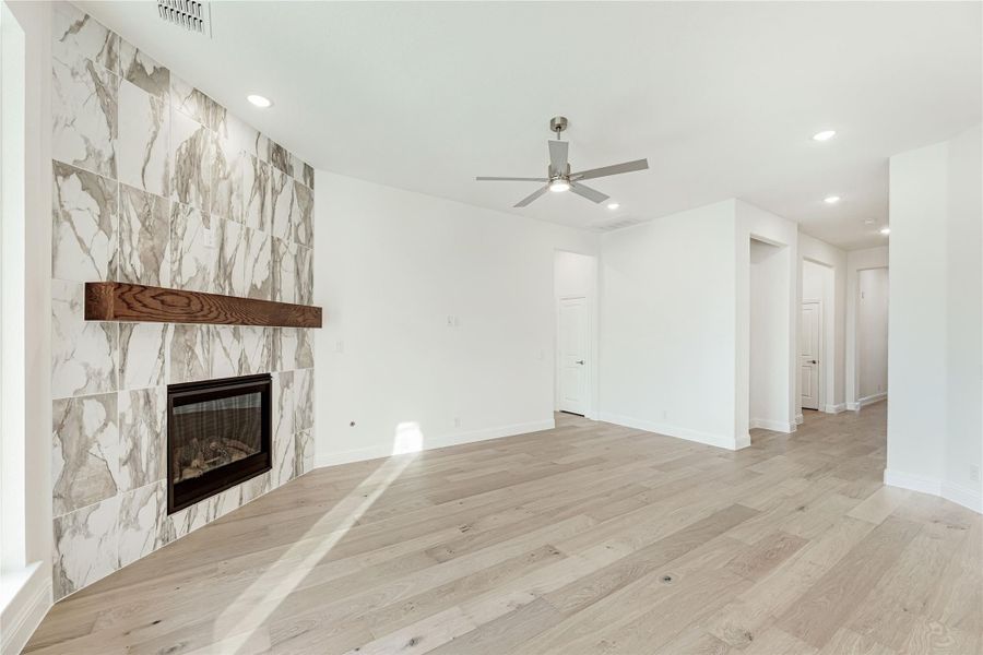 Open living room with marble tile fireplace, wood mantel, light hardwood floors, and ceiling fan