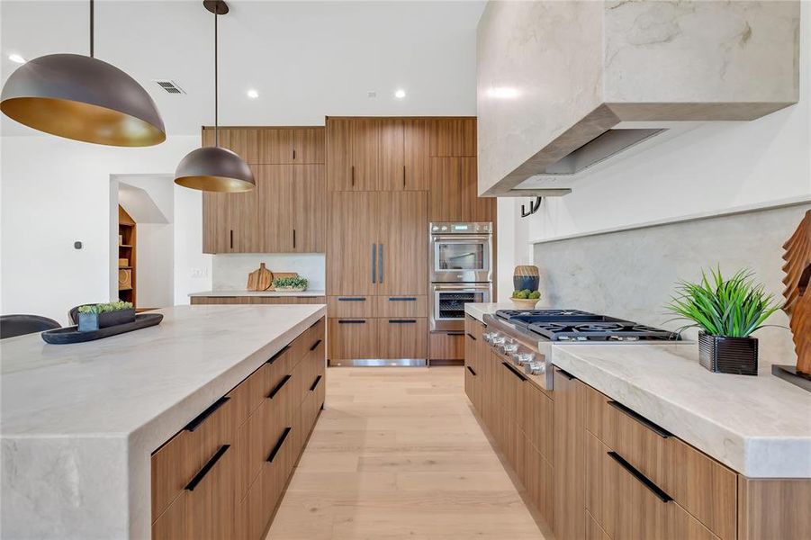 Kitchen featuring appliances with stainless steel finishes, modern cabinets, backsplash, light wood-type flooring, and light stone countertops Kitchen featuring appliances with stainless steel finishes, modern cabinets, backsplash, light wood-type flooring, and light stone countertops