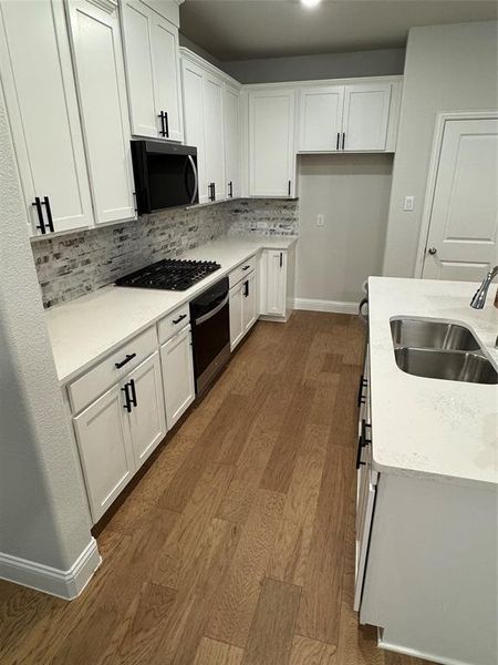 Contemporary kitchen featuring white cabinetry with matte black hardware, white countertops, a brick-patterned backsplash, and wood-finish flooring