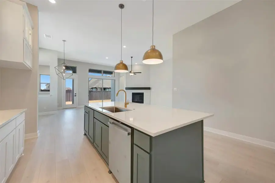 Two tone kitchen featuring a glass covered fireplace, light wood-style flooring, stainless steel dishwasher, decorative light fixtures, and an island with sink Two tone kitchen featuring a glass covered fireplace, light wood-style flooring, stainless steel dishwasher, decorative light fixtures, and an island with sink