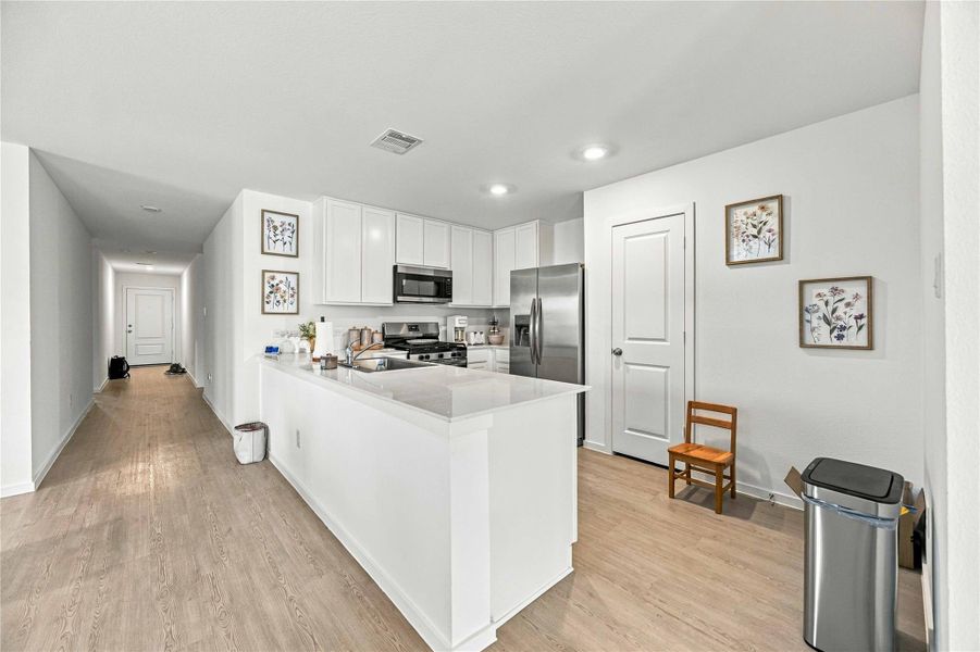 Bright and inviting kitchen featuring modern stainless steel appliances, a spacious island with ample seating, and elegant cabinetry, all complemented by sleek wood flooring.