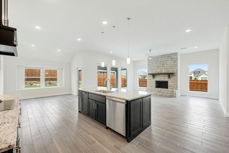 Open-concept kitchen with dark island, granite countertops, and brick fireplace in adjoining living area Open-concept kitchen with dark island, granite countertops, and brick fireplace in adjoining living area