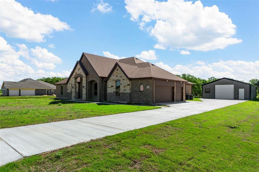 View of front of house featuring brick siding, a garage, a front lawn, roof with shingles, and an outbuilding View of front of house featuring brick siding, a garage, a front lawn, roof with shingles, and an outbuilding
