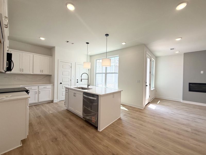 Kitchen featuring white cabinets, an island with sink, light stone counters, and hanging light fixtures