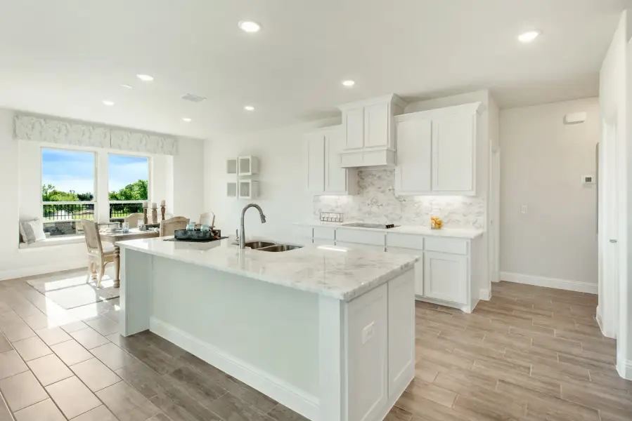 Kitchen with white cabinets, marble countertops, large island with sink, and wood-look tile floors open to dining area.