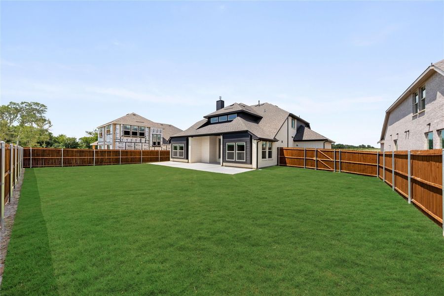 Backyard with large green lawn, wood privacy fence, and concrete patio behind two-story home