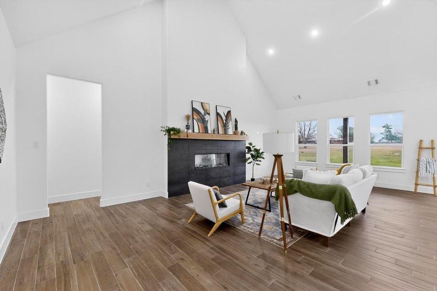 Living room with high vaulted ceiling, wood finished floors, a fireplace, and recessed lighting Living room with high vaulted ceiling, wood finished floors, a fireplace, and recessed lighting