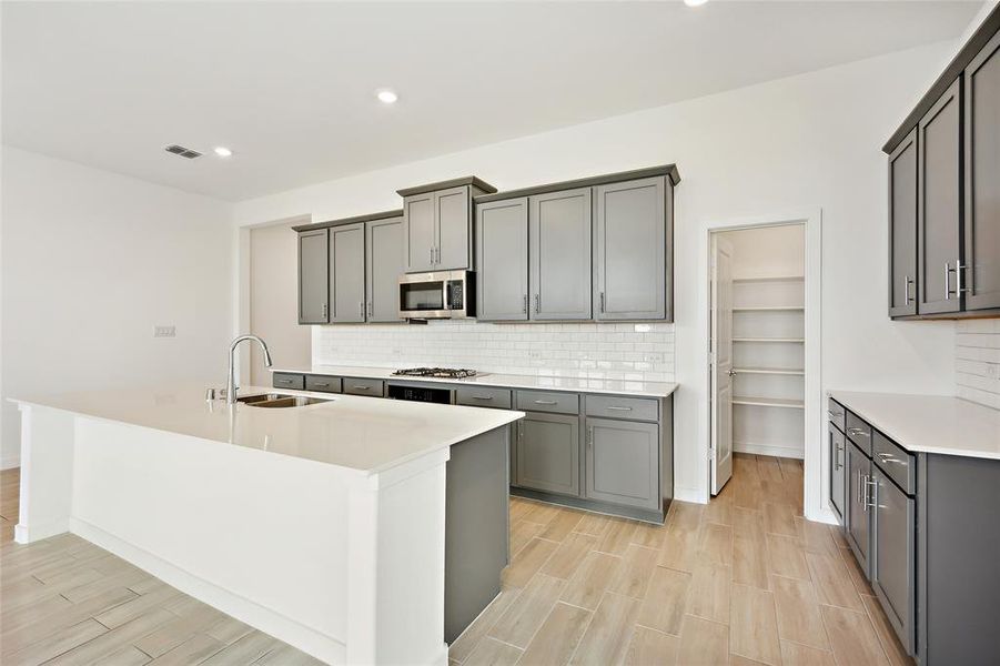 Kitchen with appliances with stainless steel finishes, a kitchen island with sink, sink, and gray cabinets