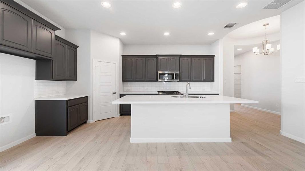 Kitchen featuring an inviting chandelier, a kitchen island with sink, and light wood-type flooring