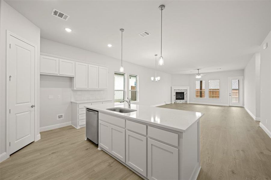 Kitchen featuring dishwasher, a fireplace, white cabinets, light wood-style floors, and recessed lighting