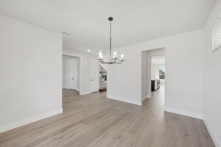 Empty dining room with light wood floors, white walls, and a chandelier overhead Empty dining room with light wood floors, white walls, and a chandelier overhead