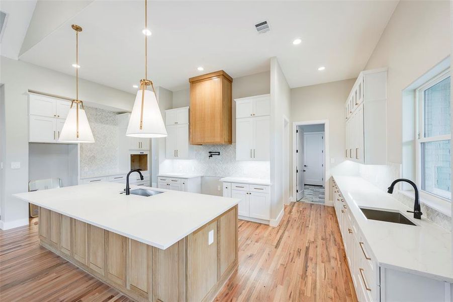 Kitchen with white cabinets, light wood finished floors, tasteful backsplash, light stone countertops, and pendant lighting