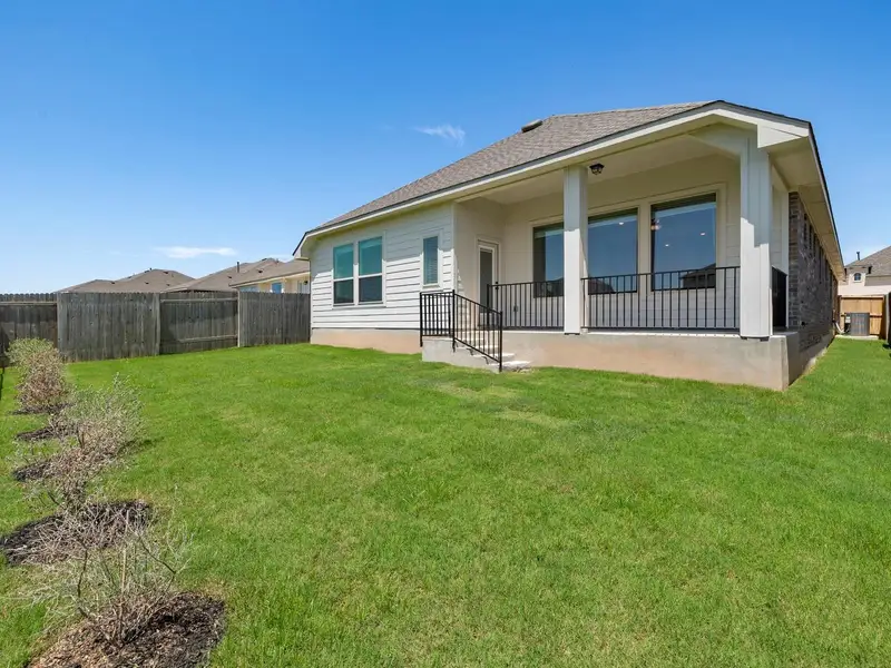 Expansive green lawn with a covered patio featuring a black metal railing, prominent support columns, and large windows