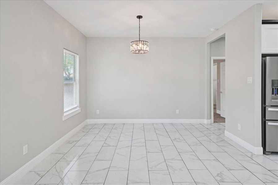 Spare room featuring light marble finish floors and a chandelier