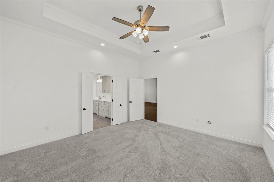 Unfurnished bedroom with a raised ceiling, ornamental molding, carpet, ensuite bathroom, and multiple windows Unfurnished bedroom with a raised ceiling, ornamental molding, carpet, ensuite bathroom, and multiple windows